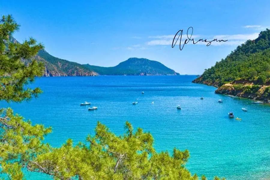 a stunning turquoise bay in adrasan, turkey, surrounded by lush green hills, with boats floating on the calm waters