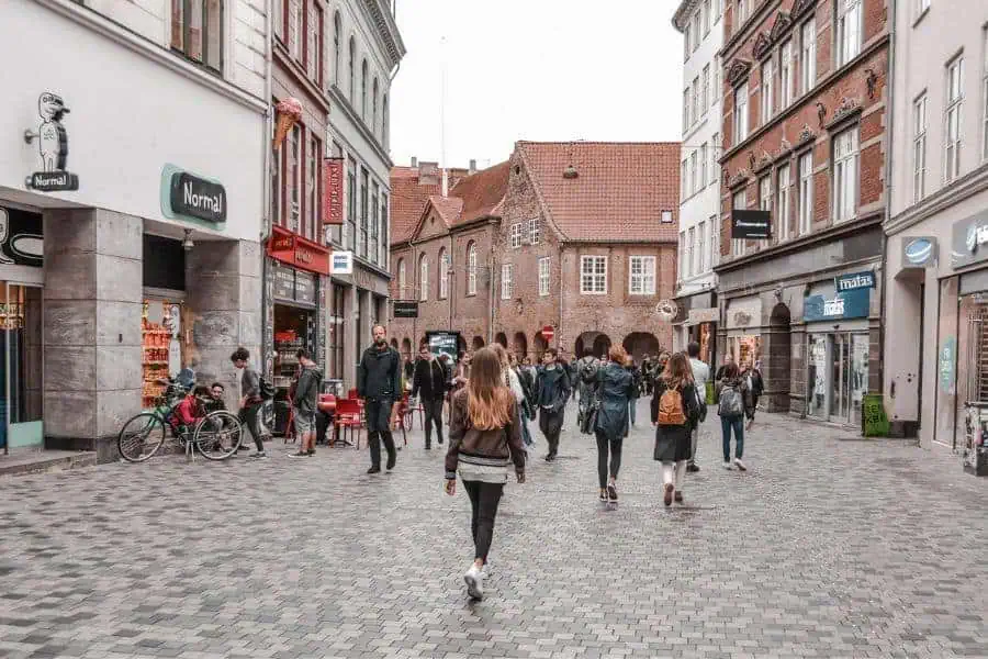 Shoppers and cyclists on the cobblestone pedestrian street of Copenhagen, lined with brick buildings and local stores: a lively stop on any Denmark itinerary