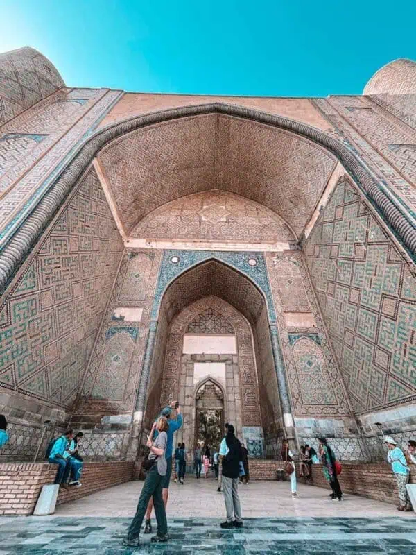 inside the grand arch of bibi khanum mosque showing detailed geometric tilework and people standing beneath the massive portal