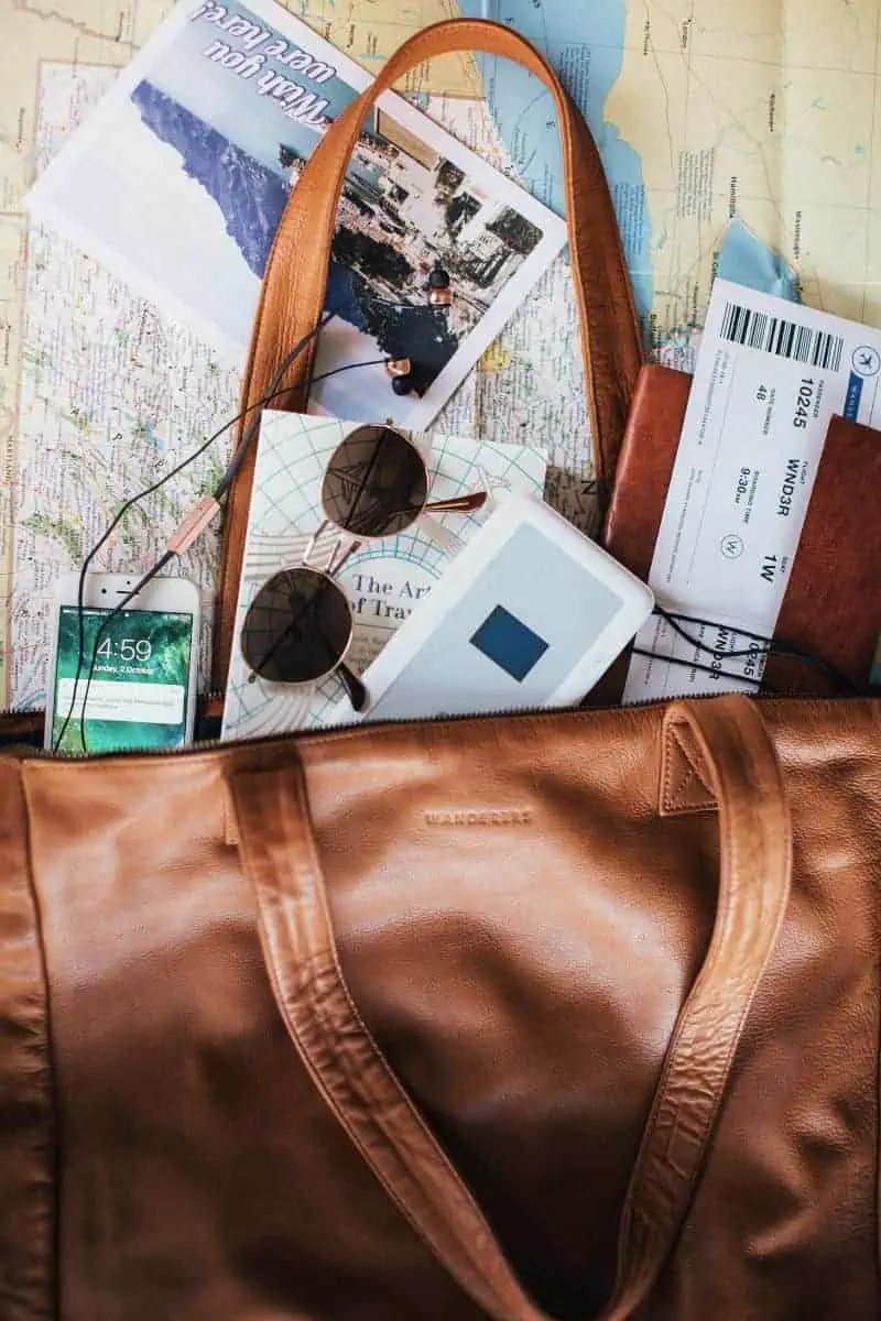 brown leather travel bag with sunglasses, phone, passport, tickets, and travel book on a map