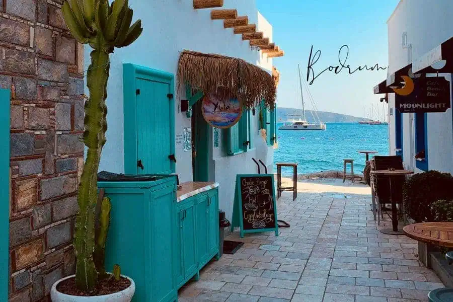 charming alleyway in bodrum with whitewashed buildings, bright turquoise doors, and a view of the aegean sea with sailboats in the distance