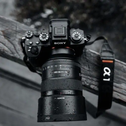 close-up of a Sony Alpha 1 camera with a zoom lens placed on a wooden railing