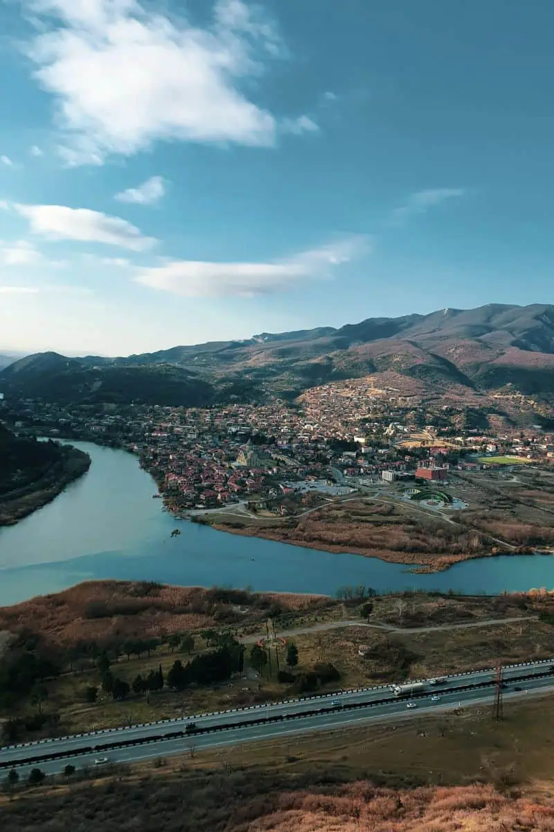 aerial view of the confluence of aragvi and mtkvari rivers at mtskheta with red-roof town nestled between the hills under a blue sky