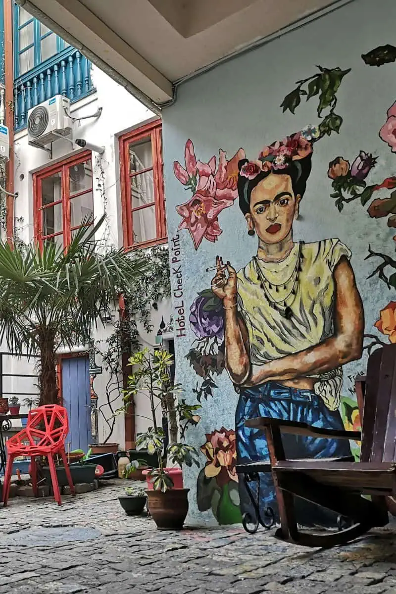 A quirky courtyard mural of Frida Kahlo at Hotel Check Point in Tbilisi, surrounded by potted plants, red chairs, and pops of color