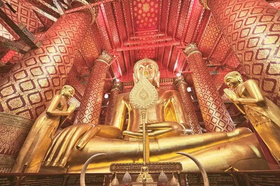 massive golden seated buddha statue inside wat phanan choeng in ayutthaya, thailand, surrounded by intricate red and gold decor with worshippers paying respect