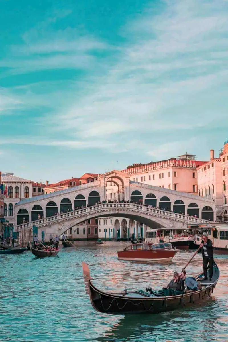 gondola with tourists floating on grand canal under the historic rialto bridge in venice, italy
