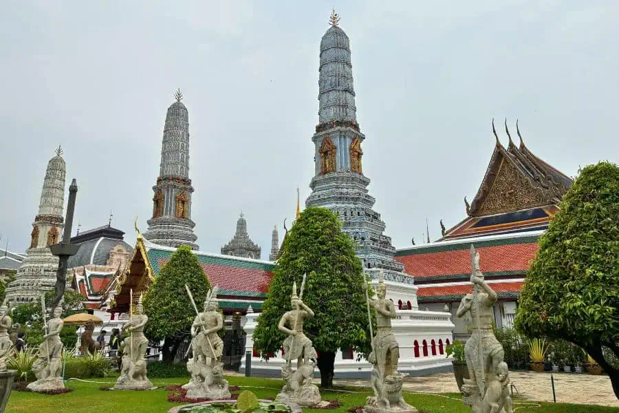 the grand palce complex  in bangkok featuring spires and white statues 