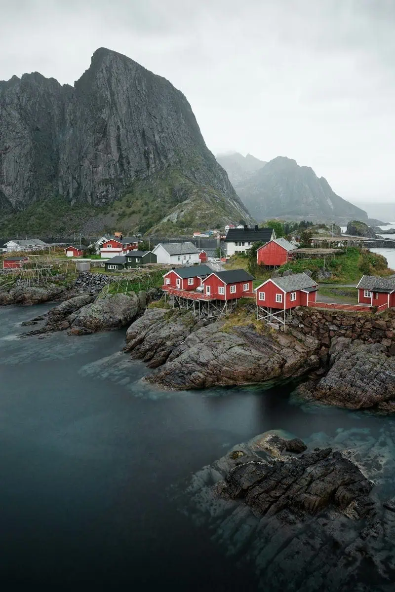 charming red cabins on rocky shoreline with towering mountains in the background, lofoten islands, norway