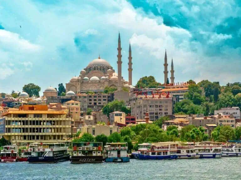 historic mosque with towering minarets overlooking the waterfront in istanbul, turkey, with colorful boats docked along the shore and a bright blue sky above