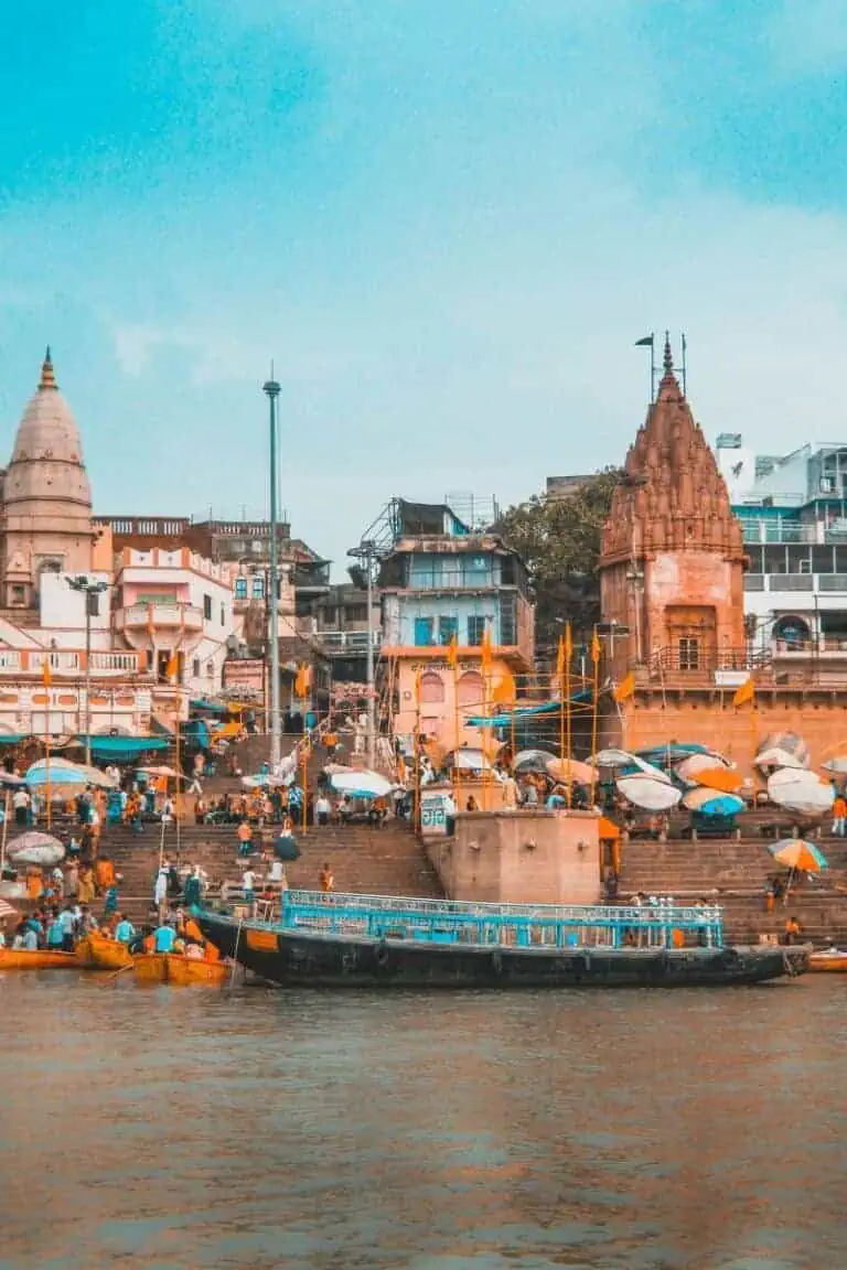 a vibrant riverside scene at one of the ghats in varanasi, india, with ancient temples, colorful umbrellas, and crowds of people gathered along the ganges river for rituals and boat rides