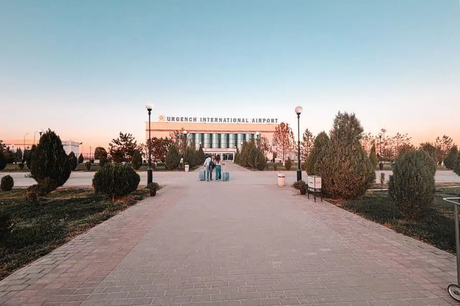 entrance walkway of urgench international airport in uzbekistan, with hubby and mini-me pulling suitcases toward the terminal building