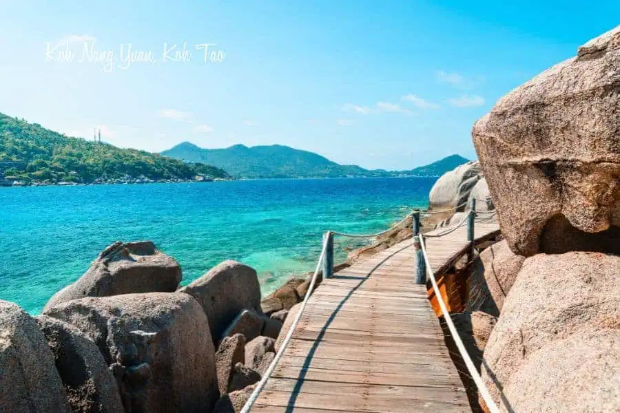 scenic wooden walkway along the rocky shoreline of koh nang yuan, near koh tao, thailand, with crystal-clear turquoise waters and lush green hills in the background