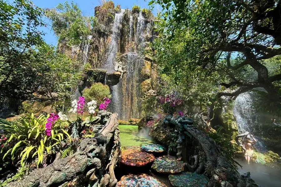 a serene scene at lalitta café in chiang rai featuring a lush garden with vibrant flowers, whimsical colorful stepping stones, and cascading waterfalls