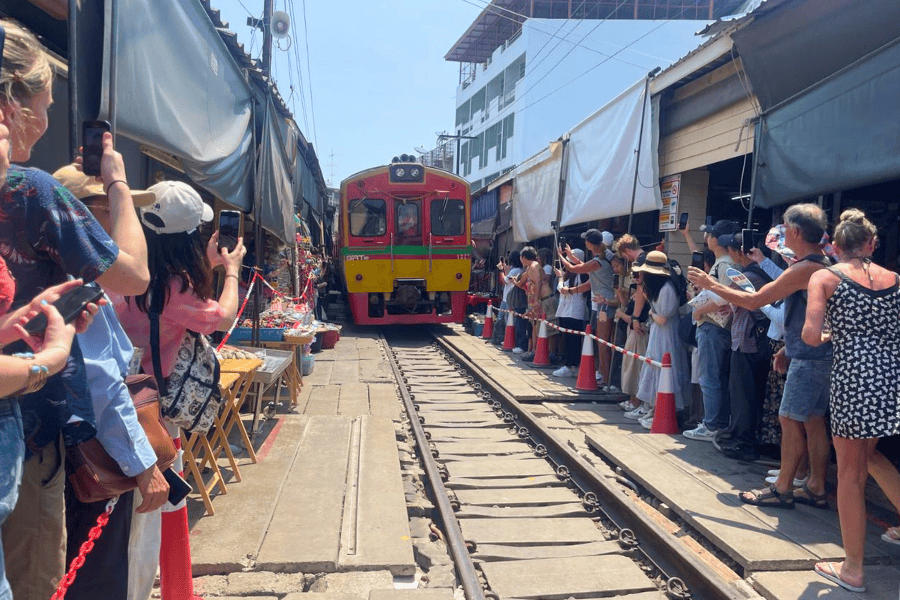 train arriving on a railway track right between the stalls at maeklong railway market aka talad rom hub near bangkok 