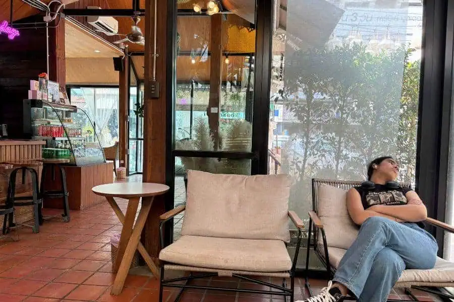 mini-me unwinding at baan buri cafe in chiang mai, thailand, with headphones around her neck, enjoying a quiet moment by the window