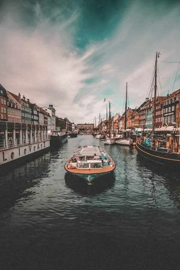 A canal boat gliding through Nyhavn, Copenhagen, with colourful historic buildings reflected in the water