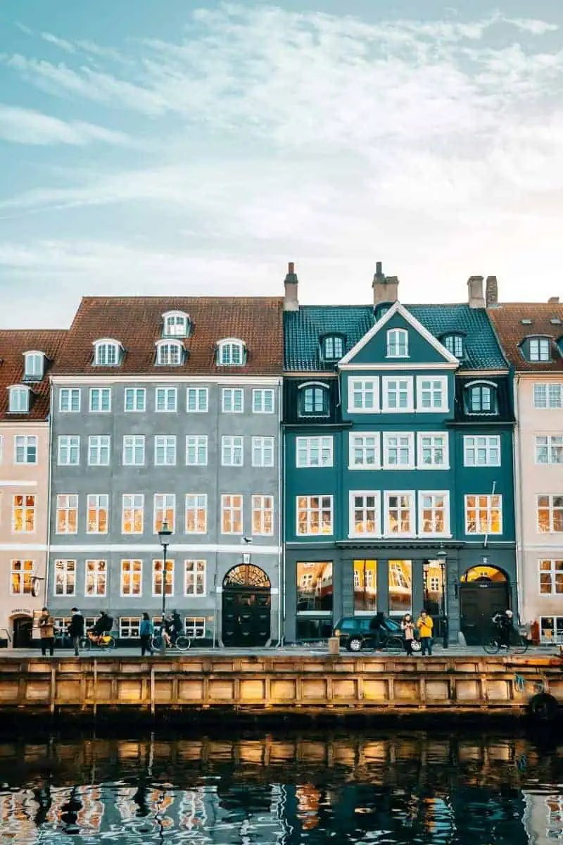 colorful traditional buildings reflected in the canal water at nyhavn, copenhagen, denmark, with people walking and cycling along the waterfront