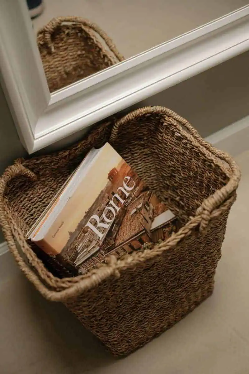 woven basket with a rome travel book placed on the floor near a white framed mirror