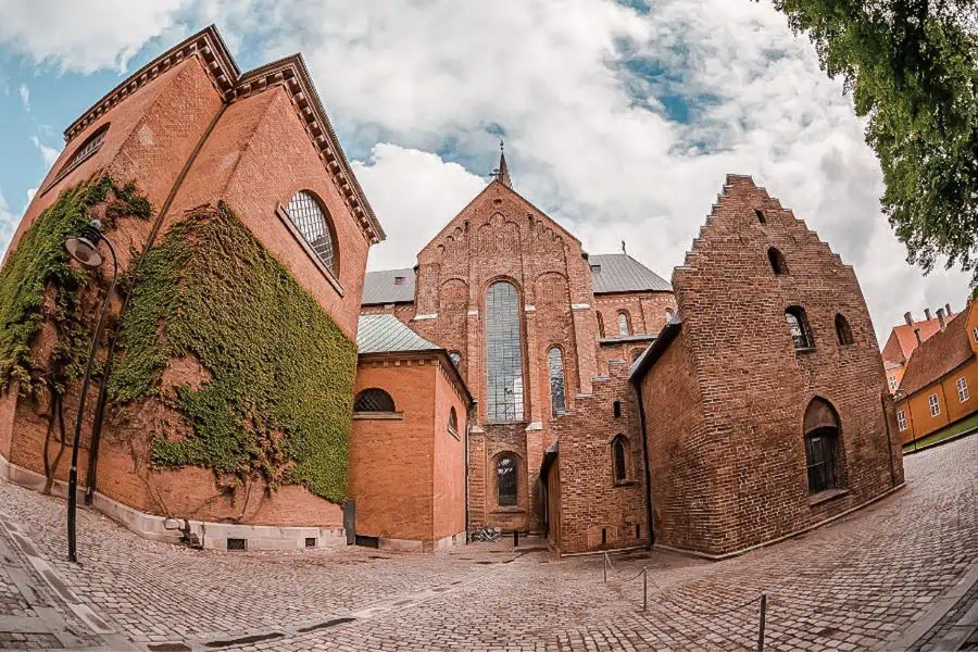 The red brick exterior of Roskilde Cathedral photographed from the cobblestone courtyard below, one of the most important churches in Denmark