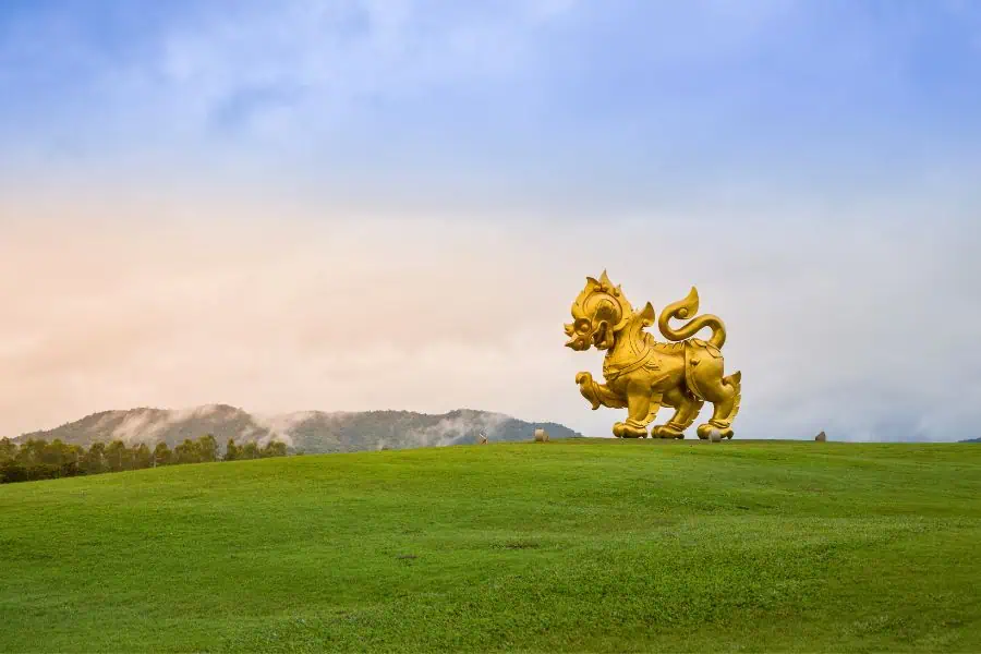 a golden statue on a green hill at singha park in chiang rai