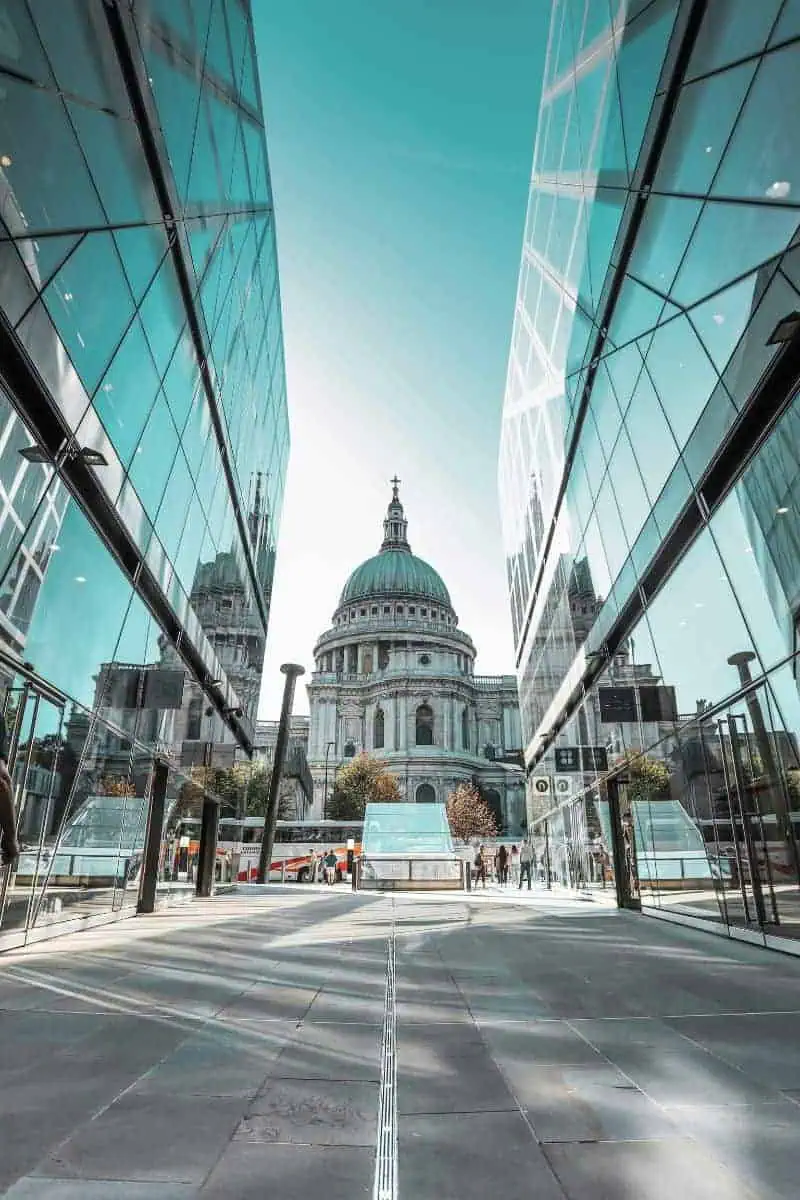 view of St. Paul’s Cathedral in London framed between two modern glass buildings, with reflections creating a symmetrical composition under a bright blue sky
