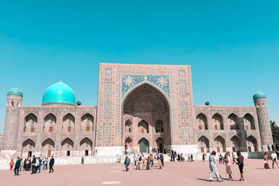 tilya-kori madrasah at registan square in samarkand with turquoise dome and visitors