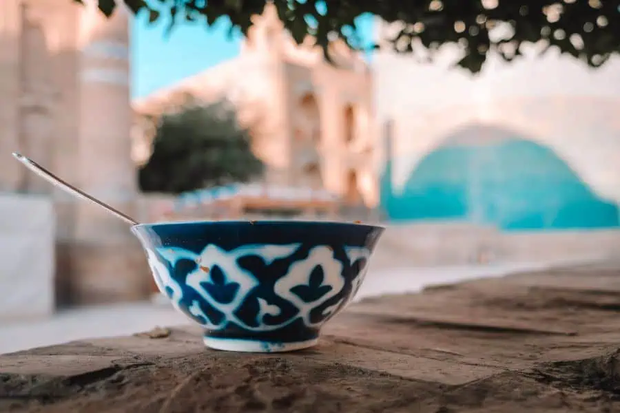 traditional uzbek ceramic bowl on wooden table in khiva with historic architecture blurred in background