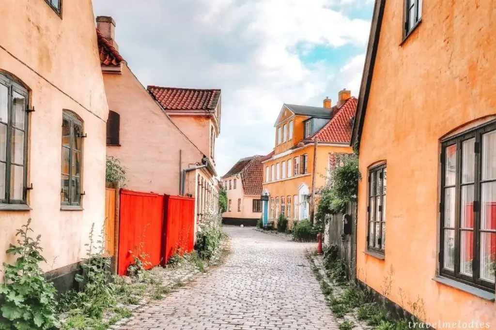 A quiet cobblestone alley flanked by yellow-painted houses and a red gate in the old town of Dragor, Denmark