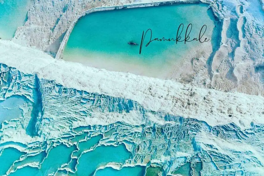 aerial view of the white travertine terraces of pamukkale with turquoise thermal pools and a small boat floating in the water