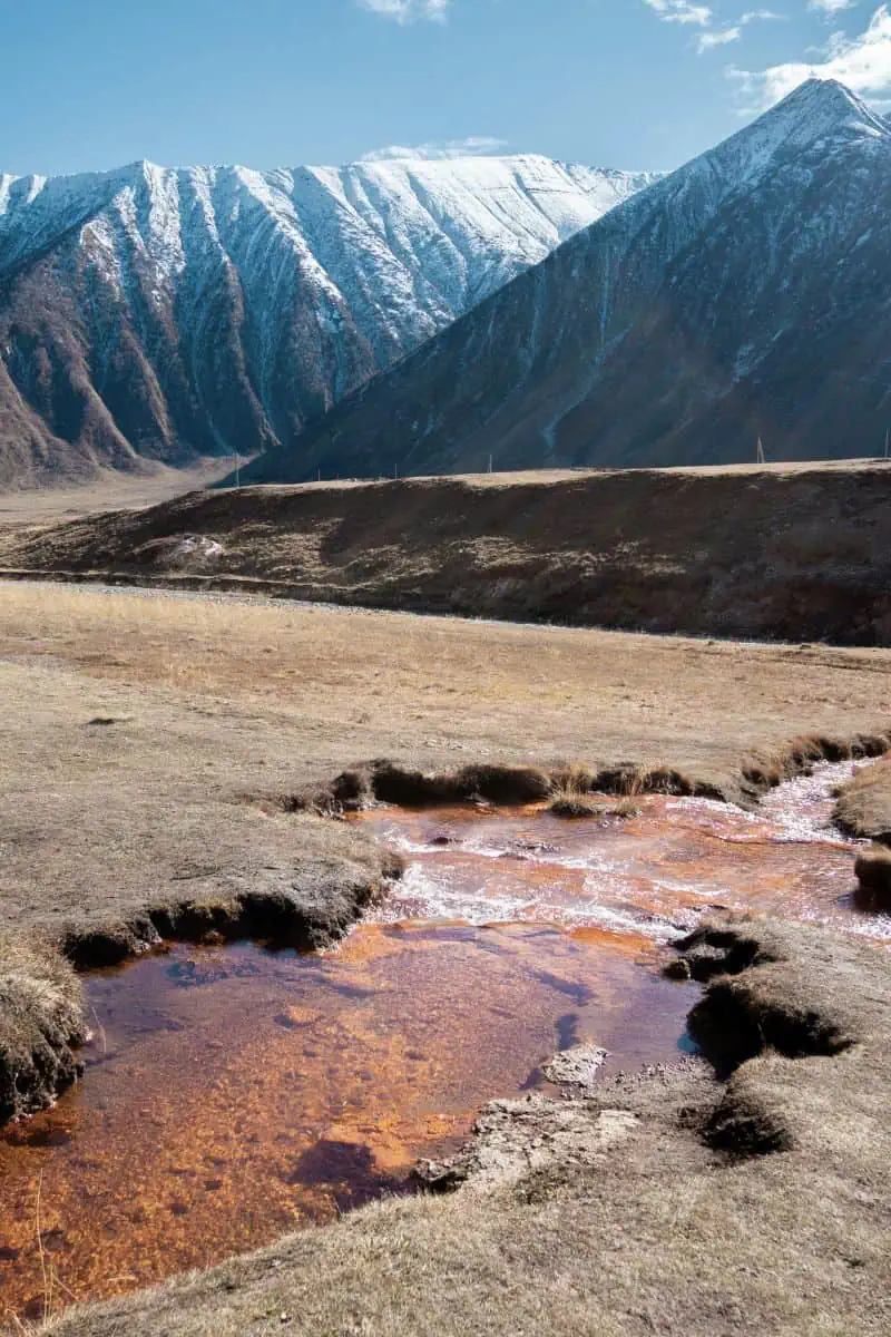 snow-capped mountains with a reddish mineral stream, terek river, flowing through a dry grass valley, trusso valley, in kazbegi, georgia