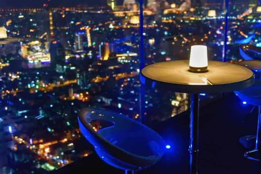 view from a high-rise rooftop bar in bangkok showing tables with a cityscape illuminated at night