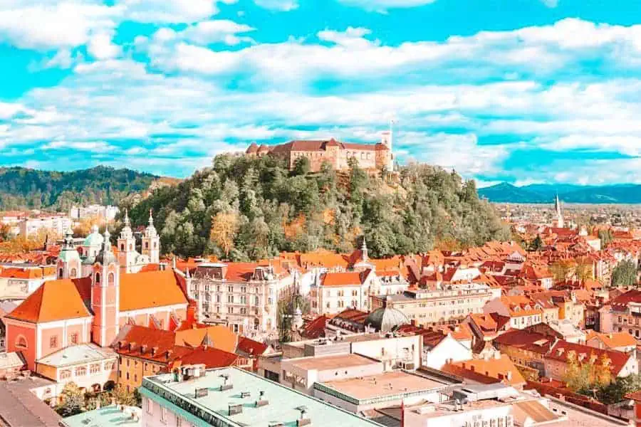 view of ljubljana castle perched on a hill and orange tile roof houses from a street in ljubljana old town