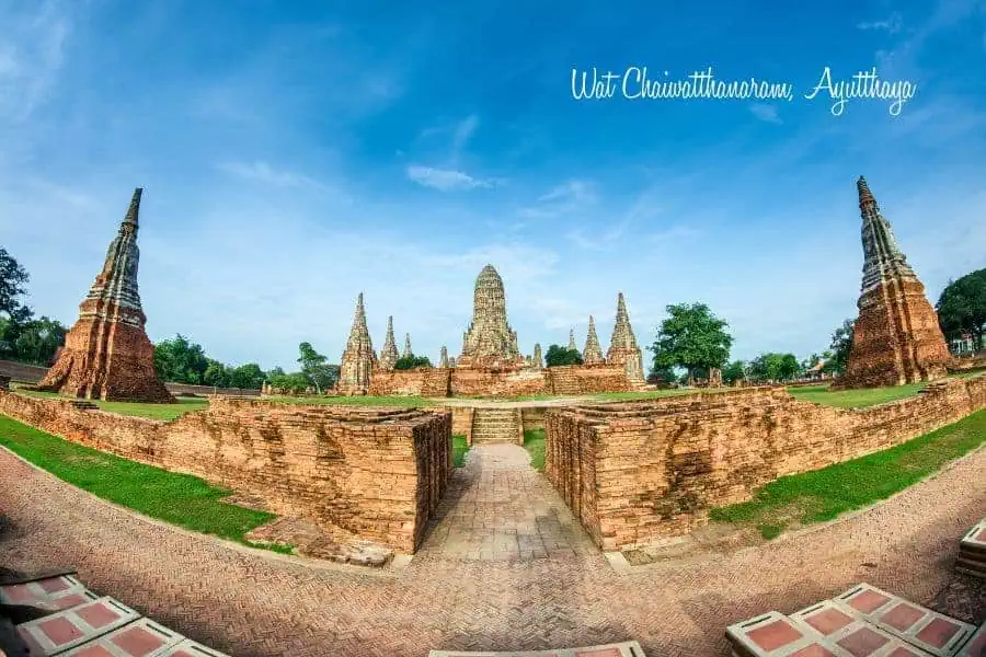 ancient ruins of wat chaiwatthanaram in ayutthaya, thailand, featuring red brick structures, towering prangs, and a bright blue sky