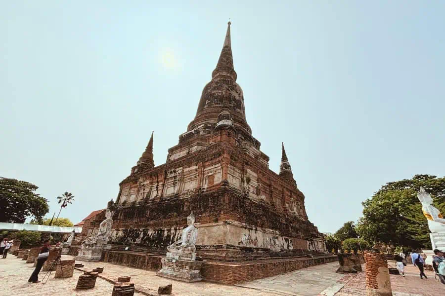 ancient stupa at wat yai chai mongkhon in ayutthaya, thailand, standing tall under the bright sun, surrounded by weathered buddha statues and scattered ruins
