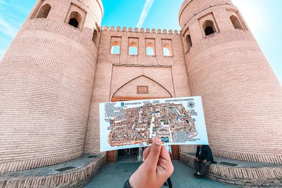 and holding a map in front of ata darwaza west gate of itchan kala khiva with twin mud brick towers