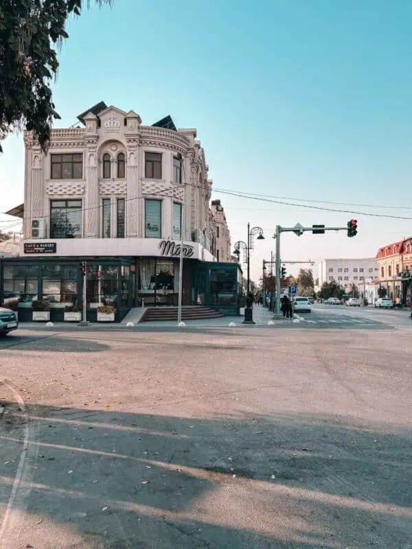 neoclassical corner building in university boulevard in samarkand city center with ornate white facade, tall arched windows, and a street-level café mone at a traffic intersection